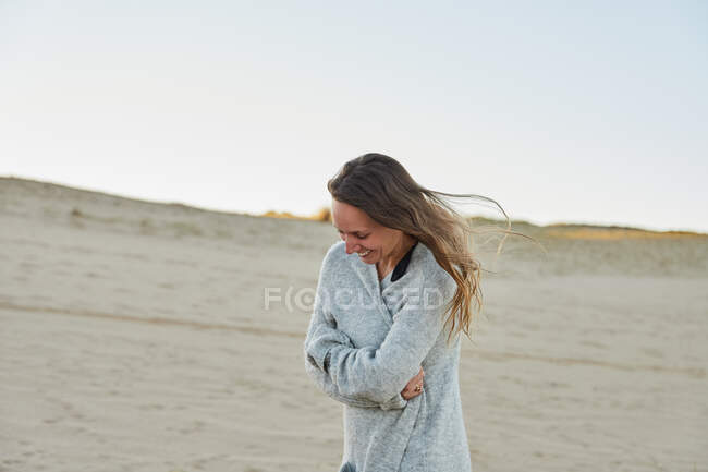 Вміст жінки в теплому одязі, що стоїть на пляжі біля моря і насолоджується літнім вечором — стокове фото
