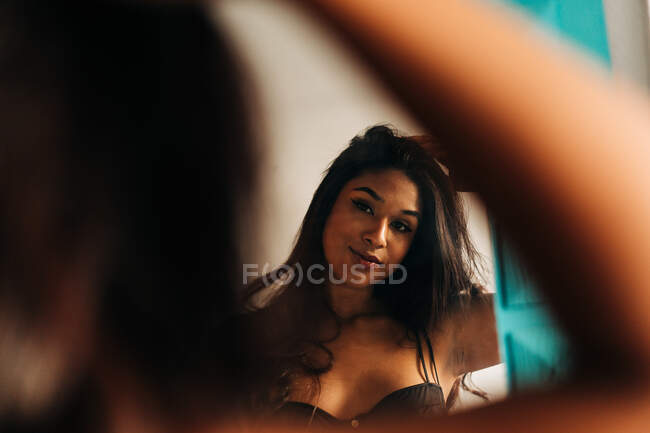 Junge hispanische Frau berührt Haare und schaut morgens zu Hause in den Spiegel — Stockfoto