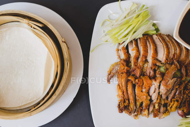 From above composition of sliced Beijing duck on white ceramic plate with traditional bamboo steamers — Stock Photo