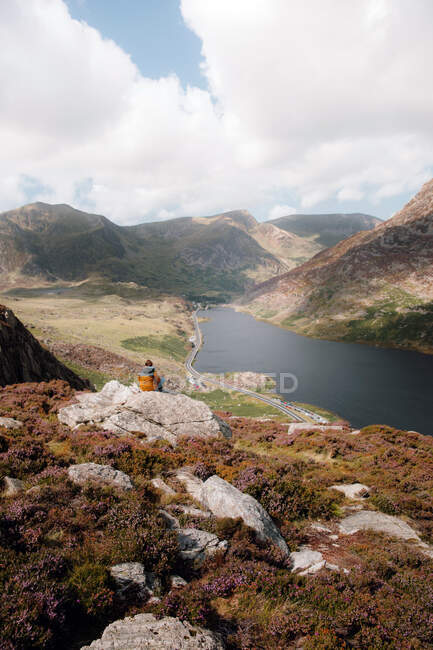 Visão traseira de fêmeas anônimas admirando colinas e rios enquanto sentadas em uma encosta acidentada durante a viagem através de Snowdonia, no interior do Reino Unido — Fotografia de Stock