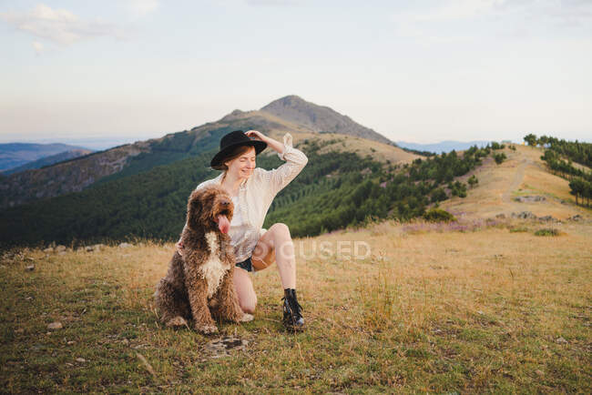 Propriétaire féminine joyeuse avec chien de hamster obéissant assis dans les montagnes détournant les yeux — Photo de stock
