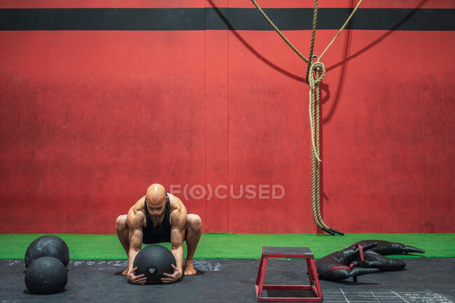Starker männlicher Athlet, der schwere Bälle vom Boden hebt, während er im modernen Fitnessstudio trainiert — Stockfoto