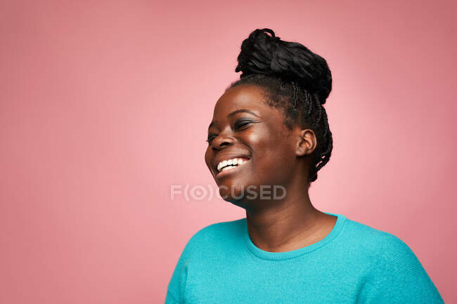 Glad African American female in blue clothes with eyes closed standing against pink background — Stock Photo