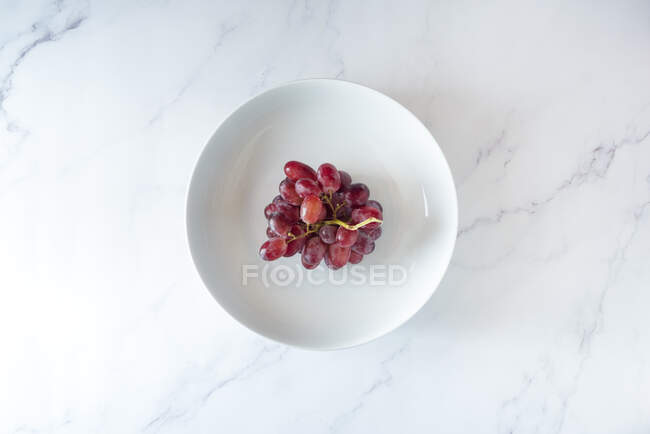 Von oben von einem Bund süßer rosa Trauben, serviert auf einem Teller auf weißem Hintergrund — Stockfoto