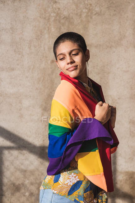 Content young bisexual ethnic female with closed eyes and multicolored flag representing LGBTQ symbols on sunny day — Stock Photo