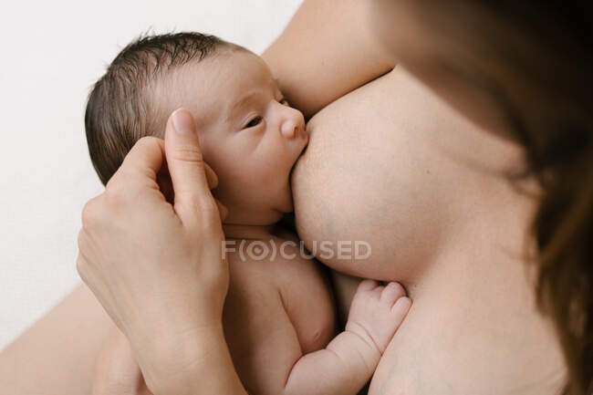 Cultivé mère aimante méconnaissable allaitement nouveau-né tout en étant assis dans la chambre à la maison — Photo de stock