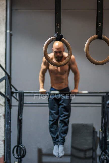 Deportista barbudo sin camisa de cuerpo completo colgado en la barra y haciendo flexiones durante el entrenamiento intenso en el gimnasio contemporáneo - foto de stock