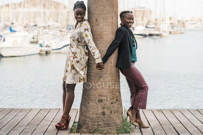 Fashionable trendy smiling African American ladies spending time together and clasping hands together in park in bright day — Stock Photo
