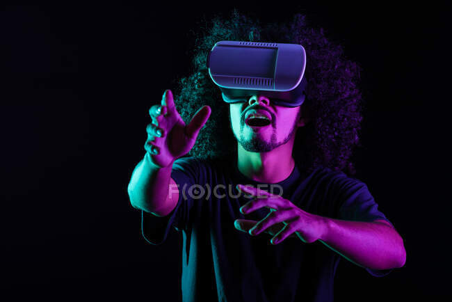 Захоплений латинським чоловіком з африканською зачіскою і в VR окуляри переживають віртуальну реальність на чорному тлі в студії з неоновими вогнями — стокове фото