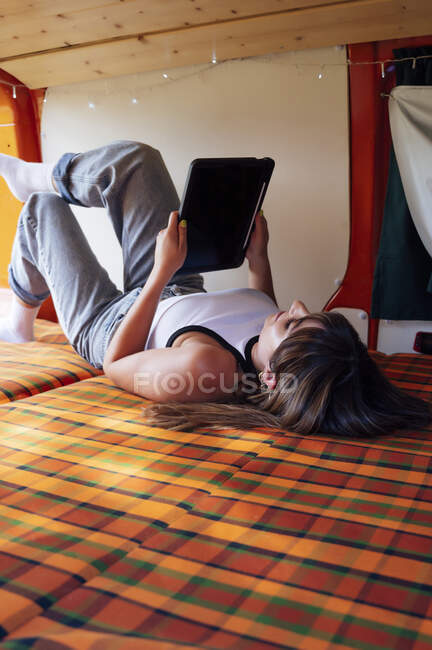 Спокійна жінка - дослідниця лежача на ліжку в фургоні і серфінг Інтернету на планшеті під час літньої подорожі. — стокове фото