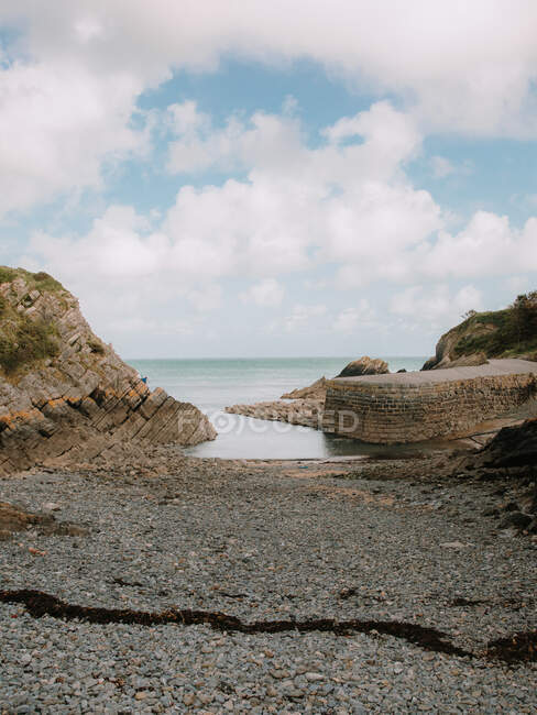 Жорстке кам'яне узбережжя спокійного моря і цегляний пірс з дорогою в похмурий день у британській природі — стокове фото