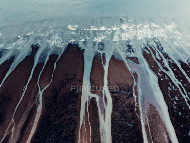 De acima da paisagem texturizada aérea de costa pedregosa desigual áspera e ondas oceânicas espumosas com fluxos — Fotografia de Stock
