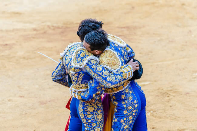 Back view of anonymous matadors in blue costumes standing on bullring and embracing after corrida performance — Stock Photo