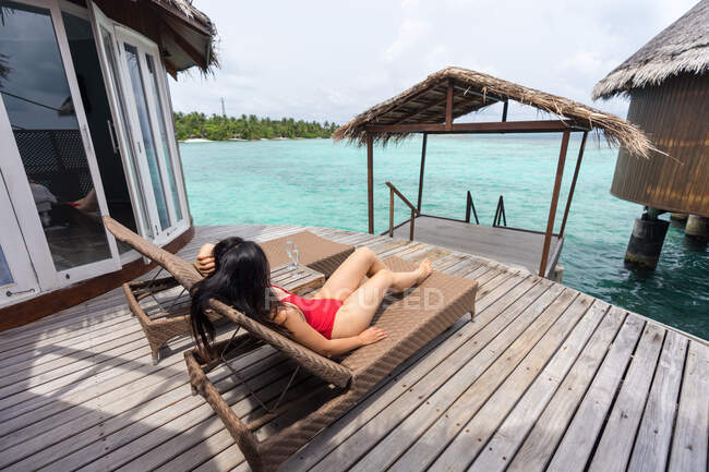 Frau mit Hand hinter dem Kopf im Badeanzug liegt auf Liegestuhl und entspannt auf den Malediven — Stockfoto
