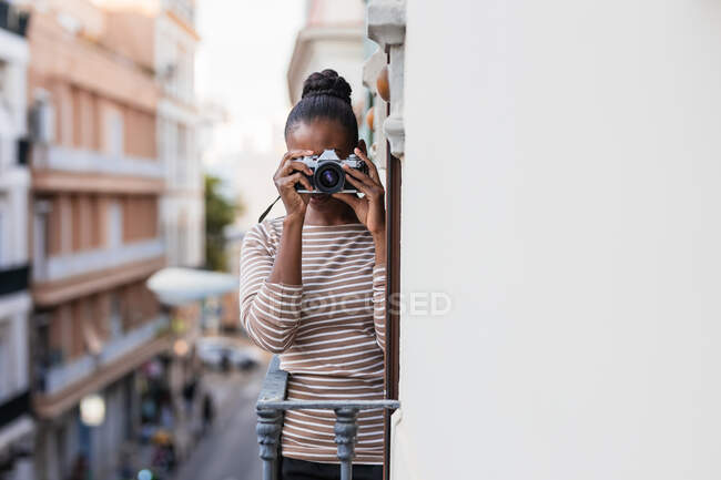 Ethnische Frau in Tracht mit gestreiftem Ornament mit professionellem Fotogerät, das tagsüber auf dem Balkon in die Kamera schaut — Stockfoto