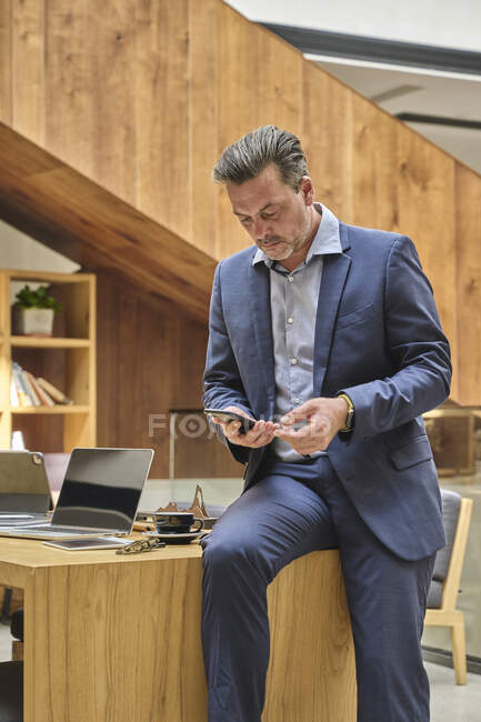 Дизайнер за рабочим столом проверяет свой смартфон во время рабочего времени — стоковое фото