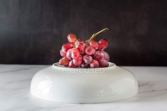 Ramo de uva rosada dulce servido en plato sobre fondo blanco - foto de stock