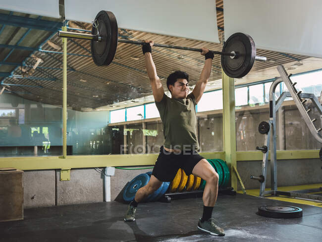 Focused Asian male athlete doing deadlift with heavy barbell during workout in gym looking away — Stock Photo