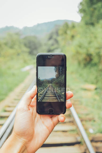 Crop hand of unrecognizable explorer taking picture of railway on mobile phone in nature — Stock Photo