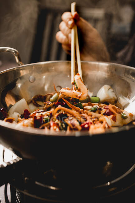 Mão cozinhar saborosa lula picante com legumes saudáveis em tigela com pauzinhos na cozinha restaurante asiático — Fotografia de Stock