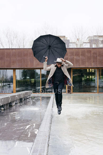 Porträt eines eleganten schwarzen Mannes mit grauem Mantel und Regenschirm auf der Straße — Stockfoto