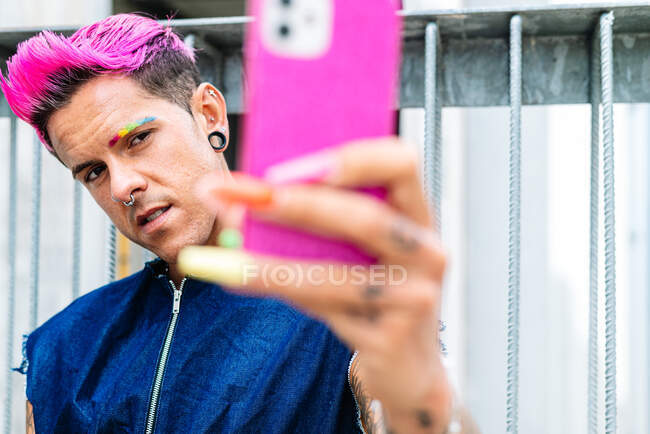 Trendy homosexual male with pink hair and colorful bight nails taking self shot on smartphone in street — Stock Photo