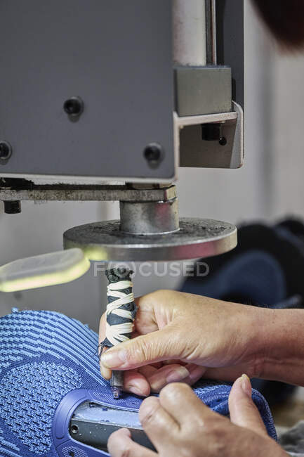 Detalle del trabajador haciendo agujeros para cordones de zapatos en fábrica de zapatos chinos - foto de stock