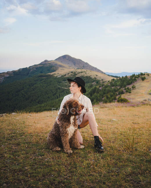Proprietária feminina com cão Labradoodle obediente sentado em montanhas olhando para longe — Fotografia de Stock