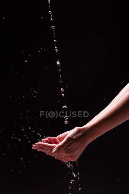 Vue de la récolte de femme anonyme se laver les mains avec de l'eau éclaboussante sur fond noir — Photo de stock