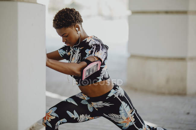 Junge, fitte Afroamerikanerin streckt Beine, bevor sie auf der Straße läuft — Stockfoto