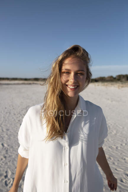 Mulher loira com cabelos longos em pé na praia olhando para a câmera — Fotografia de Stock