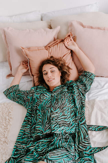 Високий кут спокійної жінки в домашньому одязі відпочиває на м'якому ліжку вдома і дивиться на камеру — стокове фото