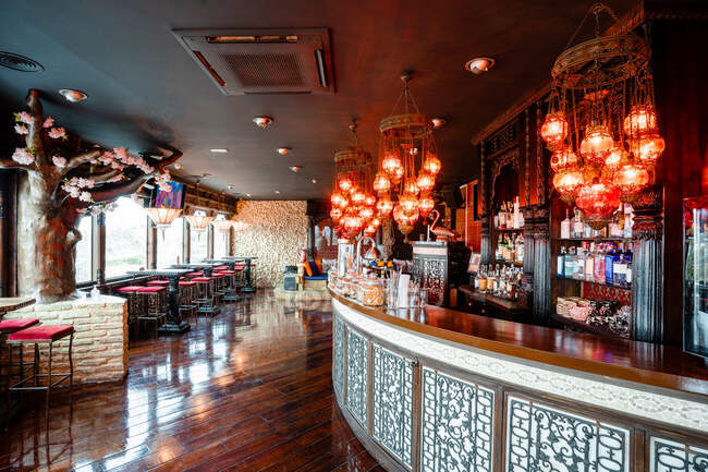 Accogliente interno di ampio bar con bancone in legno e tavoli illuminati da lampadari incandescenti — Foto stock
