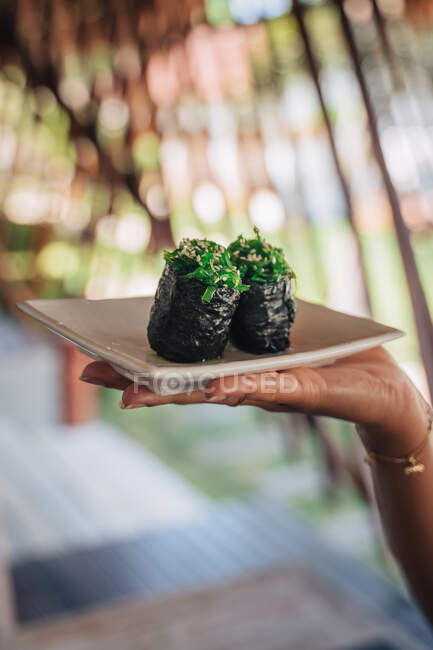 Crop unrecognizable female showing plate with delicious gunkan sushi rolls with chuka and sesame seeds in restaurant — Stock Photo