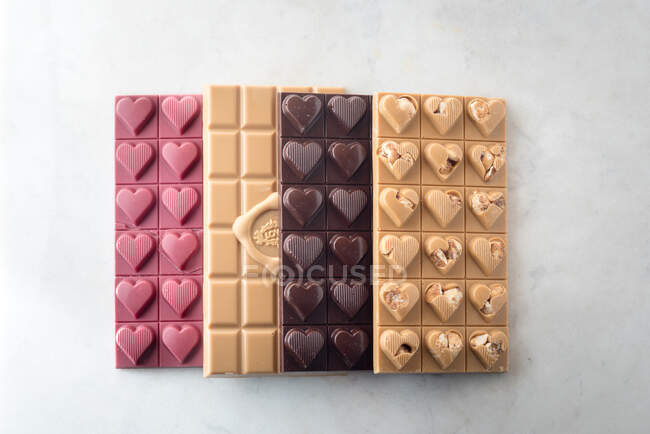 Desde arriba de deliciosas barras de chocolate coloridas colocadas en fila sobre fondo blanco - foto de stock
