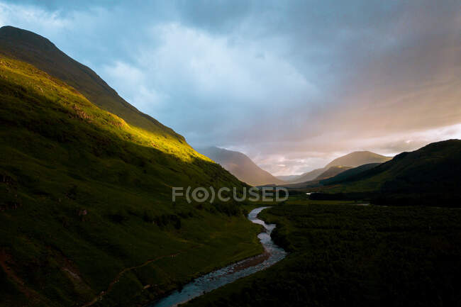 Ciel couvert au coucher du soleil sur la pente de la colline et la rivière courbée dans la soirée paisible à Glen Etive, Royaume-Uni — Photo de stock