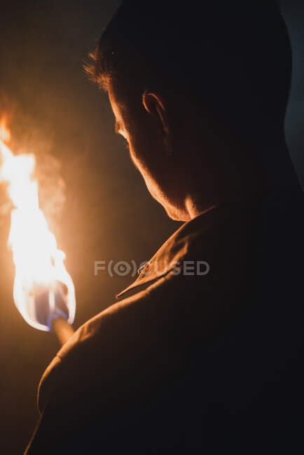 Вид сзади на обрезанный анонимный спелеолог-мужчина с пылающим факелом, стоящим в темно-узкой скалистой пещере, исследуя подземную среду — стоковое фото
