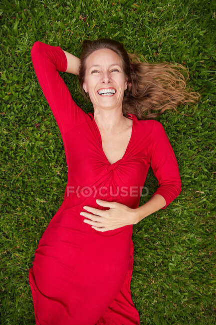 Femme vêtue de rouge couchée sur le sol dans un parc avec de l'herbe — Photo de stock