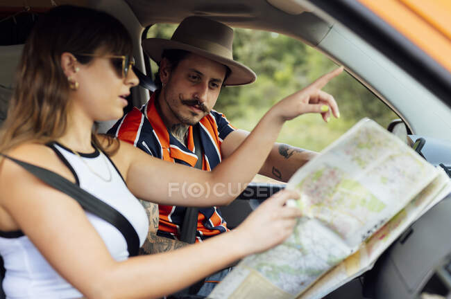 Vista lateral do casal de viajantes sentados em van e orientando com mapa de papel durante a viagem de carro no verão — Fotografia de Stock