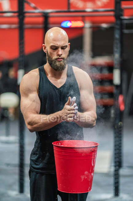 Muscular bearded guy in sportswear clapping hands and spreading powder during bodybuilding workout in gym — Stock Photo