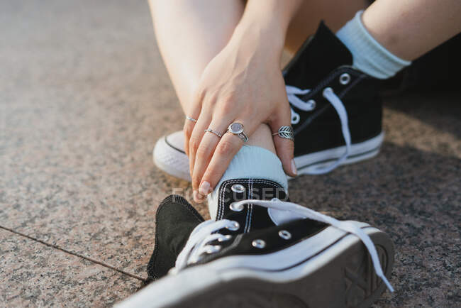 Crop unrecognizable female in silver rings and trendy footwear touching leg while sitting on walkway — Stock Photo