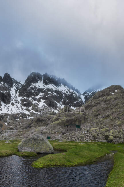 Refugio de alta montaña cerca de un lago bajo un cielo nublado - foto de stock