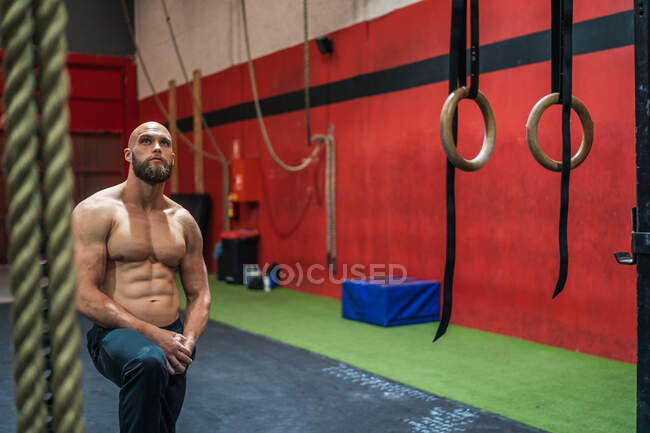 Uomo muscoloso barbuto guardando in alto mentre in piedi vicino alle attrezzature durante l'allenamento in palestra moderna — Foto stock