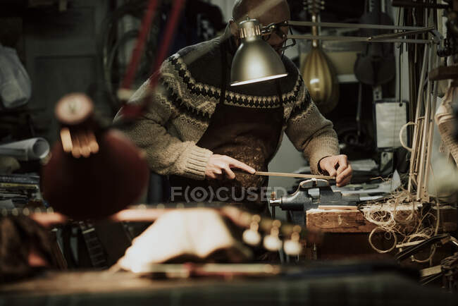 Vista lateral do artesão masculino anônimo usando pedra de moagem ao lixar pequenos detalhes de madeira da guitarra na bancada — Fotografia de Stock