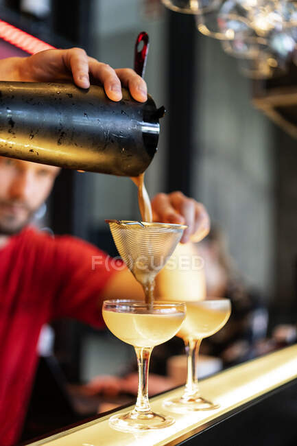 Орієнтований обрізаний невпізнаваний бармен заливає холодний освіжаючий коктейль через проціджуючий в склі, розміщений на лічильнику в барі — стокове фото