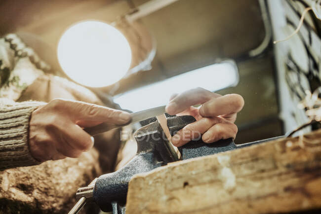 Desde abajo de la cosecha artesano masculino anónimo utilizando piedra de molienda mientras lija pequeño detalle de madera de la guitarra en el banco de trabajo - foto de stock