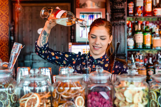 Barista donna che versa alcol nello shaker mentre prepara cocktail rinfrescanti al bancone del bar e distoglie lo sguardo — Foto stock