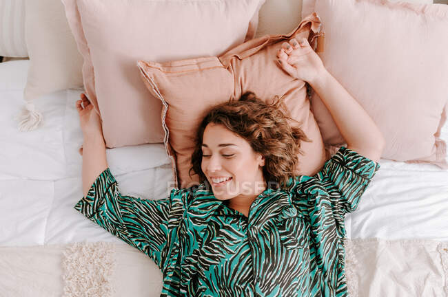 Вид зверху спокійної жінки в домашньому одязі відпочиває на м'якому ліжку вдома — стокове фото