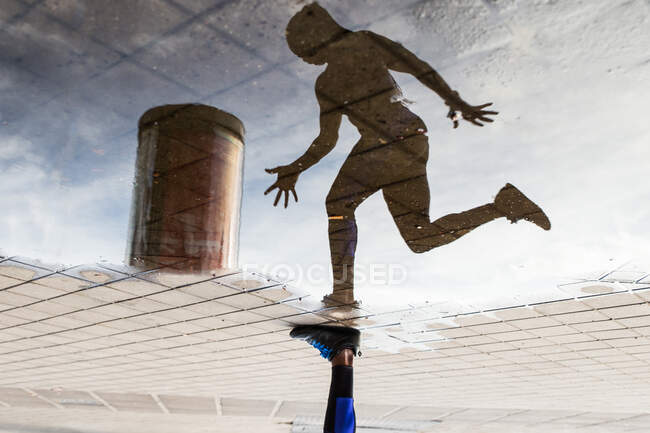 Beschnittenes Bein und Spiegelung im Wasserpaddel einer anonymen Sportlerin, die während des Outdoor-Trainings auf der Stadtstraße läuft — Stockfoto