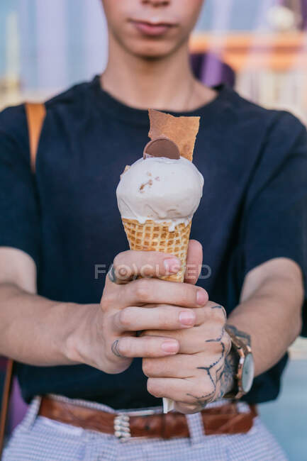 Crop tatoué main de mâle avec de la crème glacée sucrée dans un cône de gaufre dans la rue — Photo de stock